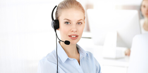 Blond woman working in sunny call center. Group of diverse people working as customer service occupation. Business concept