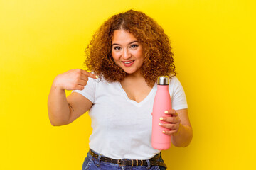 Young latin woman holding a thermos isolated on yellow background person pointing by hand to a shirt copy space, proud and confident