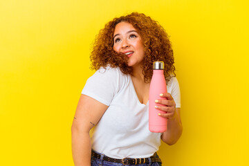 Young latin woman holding a thermos isolated on yellow background dreaming of achieving goals and purposes