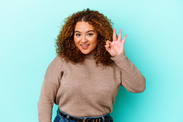 Young latin curvy woman isolated on blue background cheerful and confident showing ok gesture.