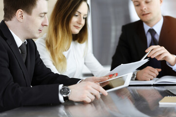 Business people or lawyers discussing questions at meeting in sunny office. Unknown businessman and woman with colleague sitting and working at the glass desk