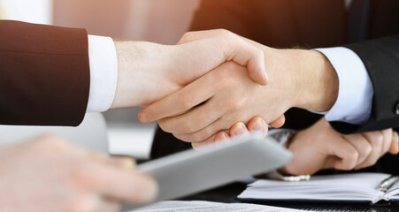 Obraz premium Businessman shaking hands with his colleague above the glass desk in sunny modern office, close-up. Unknown business people at meeting