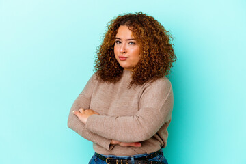 Young latin curvy woman isolated on blue background suspicious, uncertain, examining you.