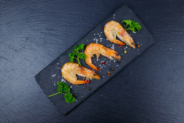 Big raw red prawns with parsley, salt and pepper on a slate board on black background. Top view