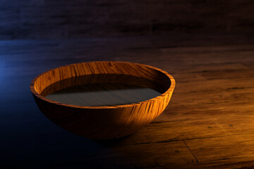 3d illustration of a round wooden bowl with water under yellow light on a dark background