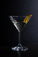 A close up of a martini glass with a drink and an orange peel in it, on a dark background.