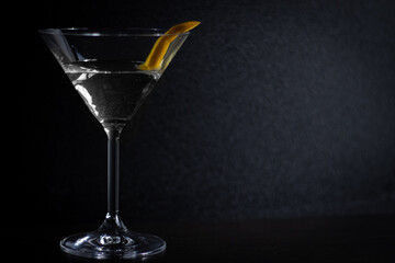 A close up of a martini glass with a drink and an orange peel in it, on a dark background.