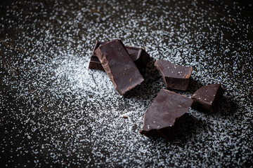 A close up of dark chocolate squares with sugar on a dark wooden table.