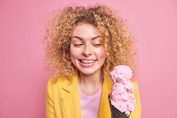 Indoor shot of good looking cheerful European woman smiles happily looks at appetizing pink ice...