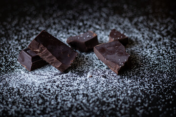 A close up of dark chocolate squares with sugar on a dark wooden table.