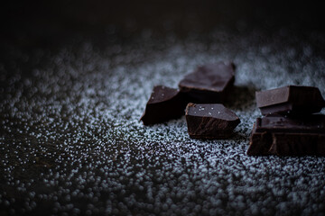 A close up of dark chocolate squares with sugar on a dark wooden table.