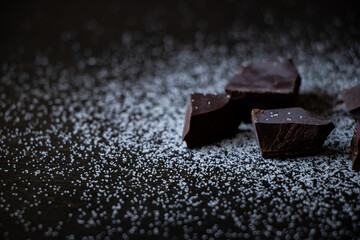 A close up of dark chocolate squares with sugar on a dark wooden table.