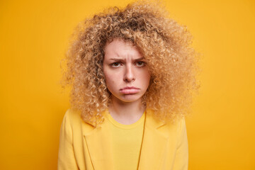 Portrait of sad unhappy young European woman with natural curly hair sulks from something unfair...