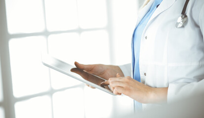 Fototapeta premium Unknown woman-doctor standing in clinic and using tablet pc, close-up. Data in medicine and healthcare