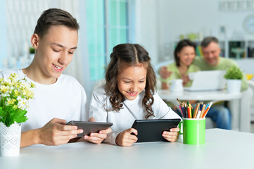 Brother and sister sitting at table and using digital devices