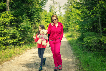 Mother and daughter on the relaxing spring walk through the green forest.