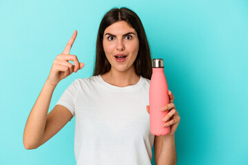 Young caucasian woman holding water bottle isolated on blue background having an idea, inspiration...