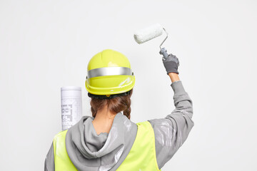 Back view of professional architect busy with design development holds architectural blueprint paints walls with roller wears protective helmet uniform isolated on white background develops new ideas