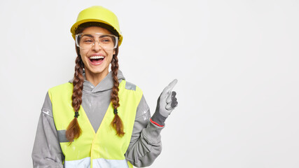 Positive woman builder on construction site demonstrates something over blank space wears hard hat protective glasses uniform has engineering career isolated over white background. Safety apparel - Powered by Adobe
