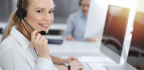 Call center. Group of casual dressed operators at work. Blond business woman in headset at customer service office. Telesales in business