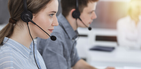 Call center. Group of casual dressed operators at work. Brunette business woman in headset at customer service office
