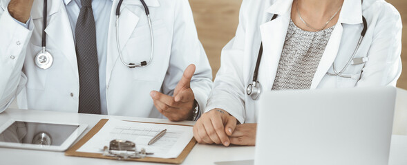 Two unknown doctors discussing treatment problems while sitting at the desk in hospital office, close-up. Data in medicine
