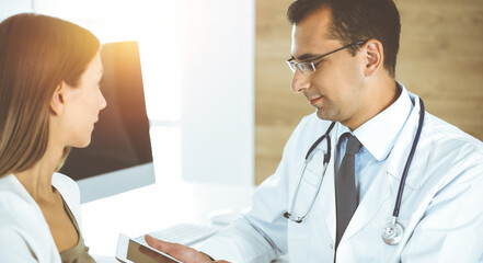 Fototapeta premium Doctor and patient discussing medical exam results while sitting at the desk in sunny clinic