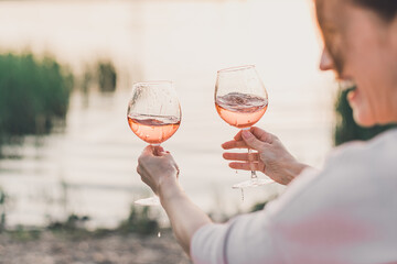 Two glasses of rose wine in female hands against the seashore.