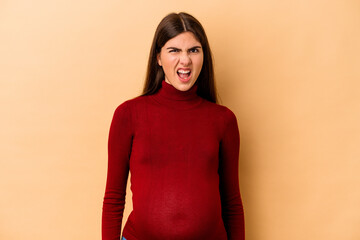 Obraz premium Young caucasian pregnant woman isolated on beige background screaming very angry and aggressive.