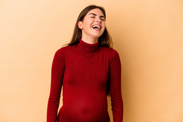 Obraz premium Young caucasian pregnant woman isolated on beige background relaxed and happy laughing, neck stretched showing teeth.