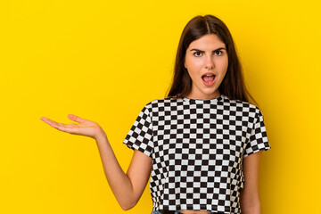Young caucasian woman isolated on yellow background impressed holding copy space on palm.