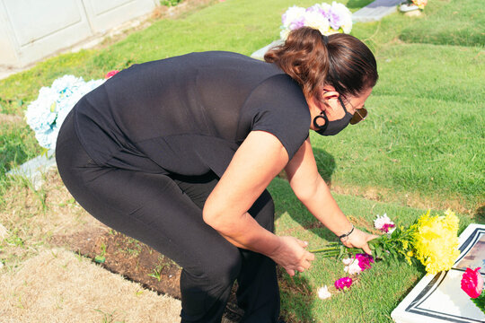 Older woman visiting a loved one at the cemetery paying respects with fresh yellow flowers. Female grieving at graveyard.