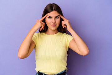 Young caucasian woman isolated on purple background focused on a task, keeping forefingers pointing head.