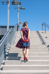 back of blonde woman in red dress walking up stairs outside