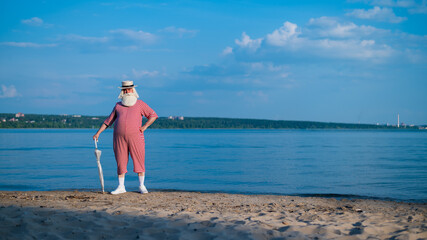 An elderly man in a classic bathing suit walks along the beach with an umbrella on a hot summer day