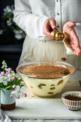 Process of making tiramisu . Sprinkling cacao powder on top of tiramisu dessert. 