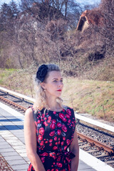 blonde woman in a red dress waiting at train station