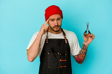 Young tattooed barber man isolated on blue background pointing temple with finger, thinking, focused on a task.