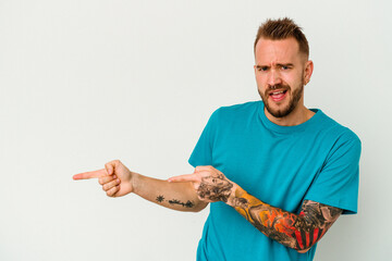 Young tattooed caucasian man isolated on white background pointing with forefingers to a copy...