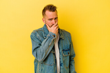 Young tattooed caucasian man isolated on yellow background covering mouth with hands looking worried.