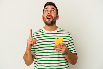 Fototapeta premium Young caucasian man holding a mobile phone isolated on white background pointing upside with opened mouth.
