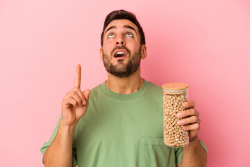 Young caucasian man holding a chickpea bottle isolated on pink background pointing upside with opened mouth.