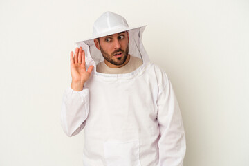 Young apiculture caucasian man isolated on white background trying to listening a gossip.