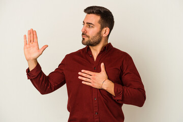 Young caucasian man isolated on white background taking an oath, putting hand on chest.