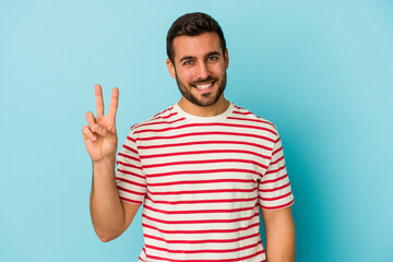 Fototapeta premium Young caucasian man isolated on blue background showing victory sign and smiling broadly.
