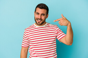Fototapeta premium Young caucasian man isolated on blue background person pointing by hand to a shirt copy space, proud and confident