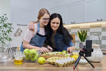 Mom and teen daughter cooking apple pie together, looking at smartphone screen