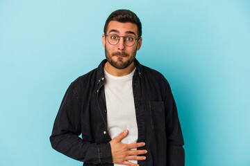 Obraz premium Young caucasian man isolated on blue background touches tummy, smiles gently, eating and satisfaction concept.