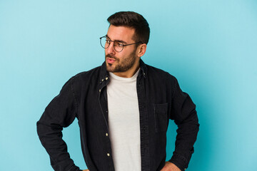 Fototapeta premium Young caucasian man isolated on blue background looks aside smiling, cheerful and pleasant.