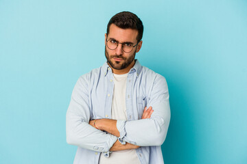 Young caucasian man isolated on blue background frowning face in displeasure, keeps arms folded.